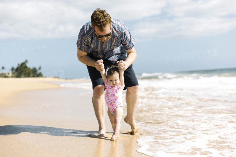 Father helping his baby girl walk on beach