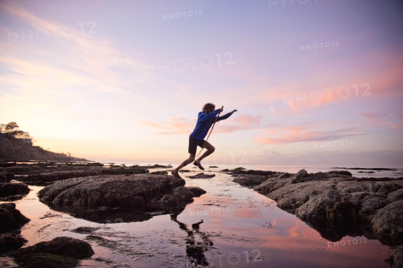 Teenage boy jumping between rocks of tide pool in La Jolla, California
