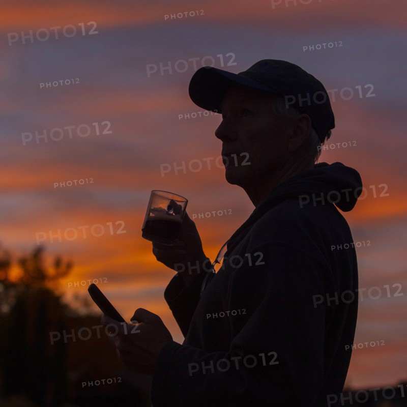 Silhouette of man holding coffee cup and smart phone at sunset