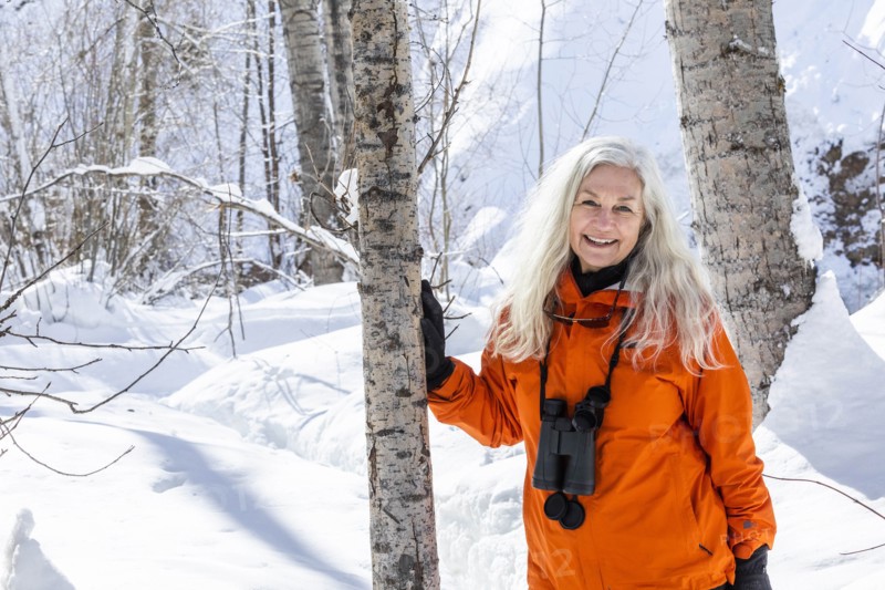 Mature woman wearing orange coat by bare trees in snow