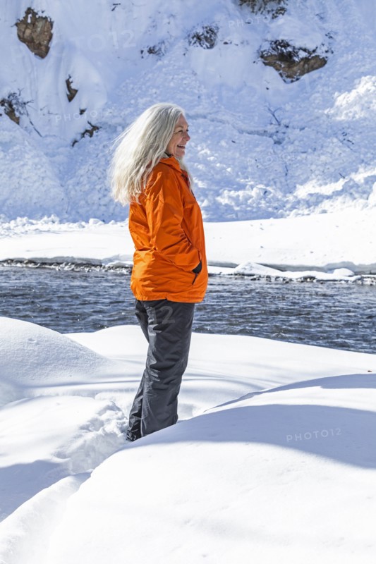Mature woman wearing orange coat on snow by river