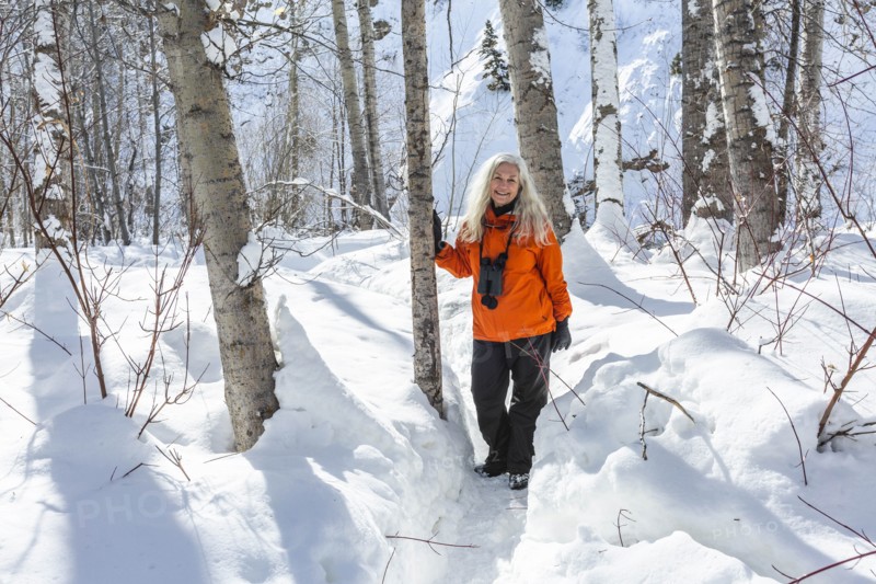 Mature woman wearing orange coat by bare trees in snow