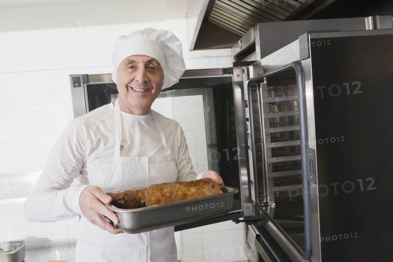 Chef holding meat in roasting tray by oven