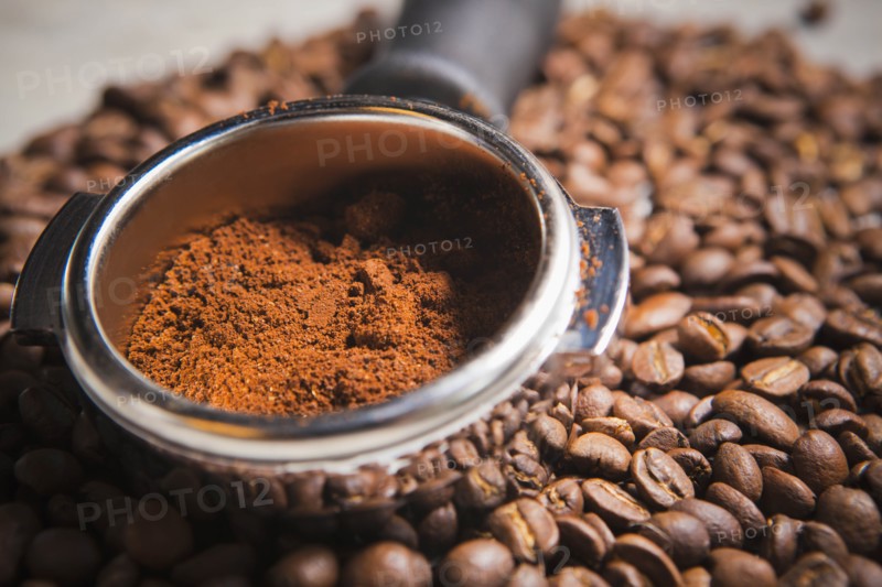 Portafilter holding ground coffee on roasted coffee beans