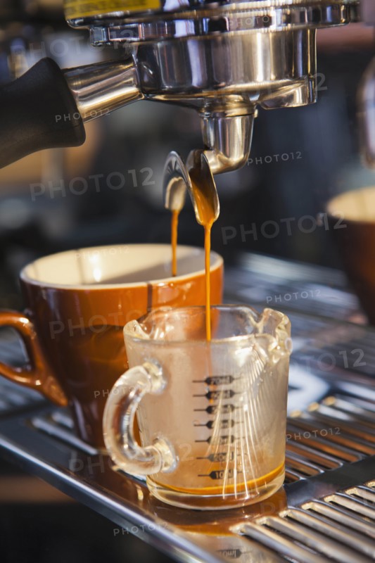 Coffee pouring from portafilter into coffee cup and beaker