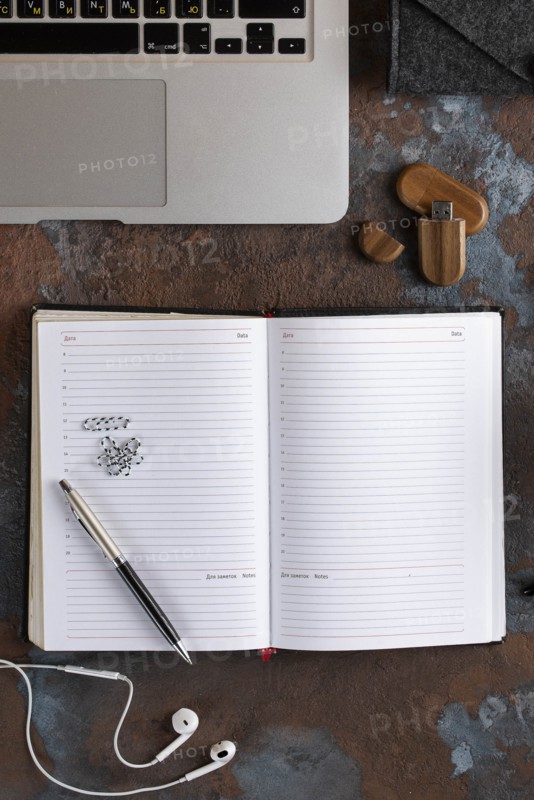 Open notebook by laptop with earbuds and USB stick