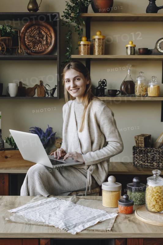 Smiling young woman using laptop in kitchen