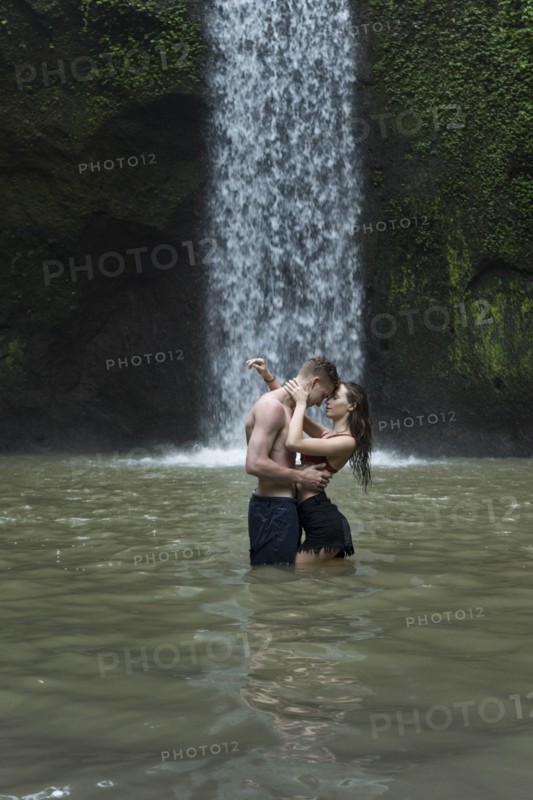 Young couple embracing in river by Tibumana Waterfall in Bali, Indonesia