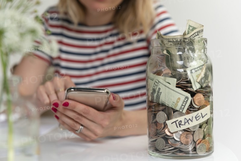 Woman using smart phone by travel saving jar