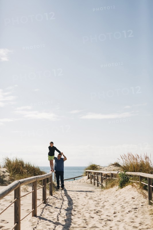 Father helping his son walking on fence on beach
