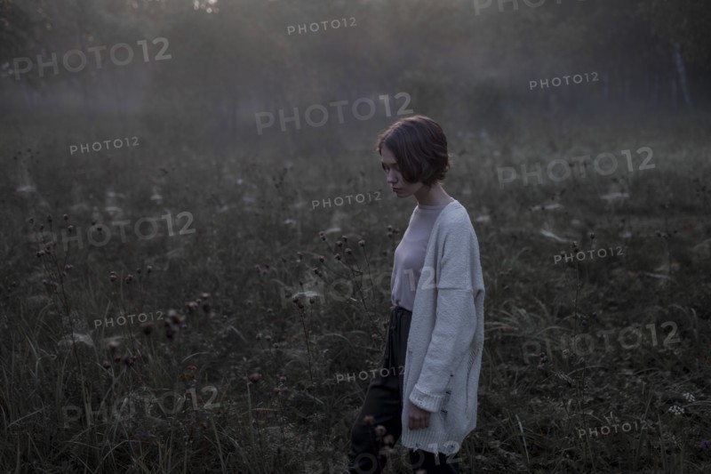Young woman wearing white cardigan in field at sunset