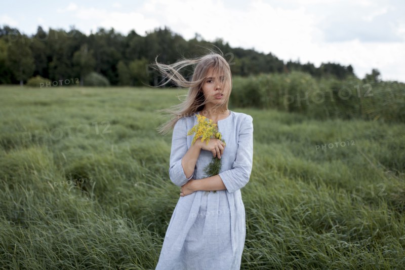 Windswept woman holding yellow flowers in field