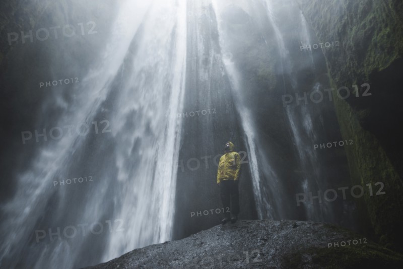 Man wearing yellow raincoat by Seljalandsfoss waterfall in Iceland