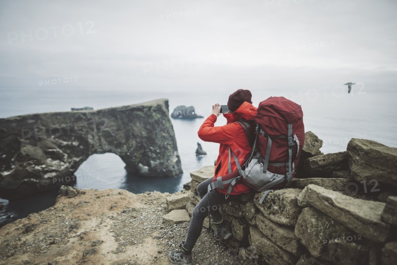 Female hiker photographing natural arch in Vik, Iceland