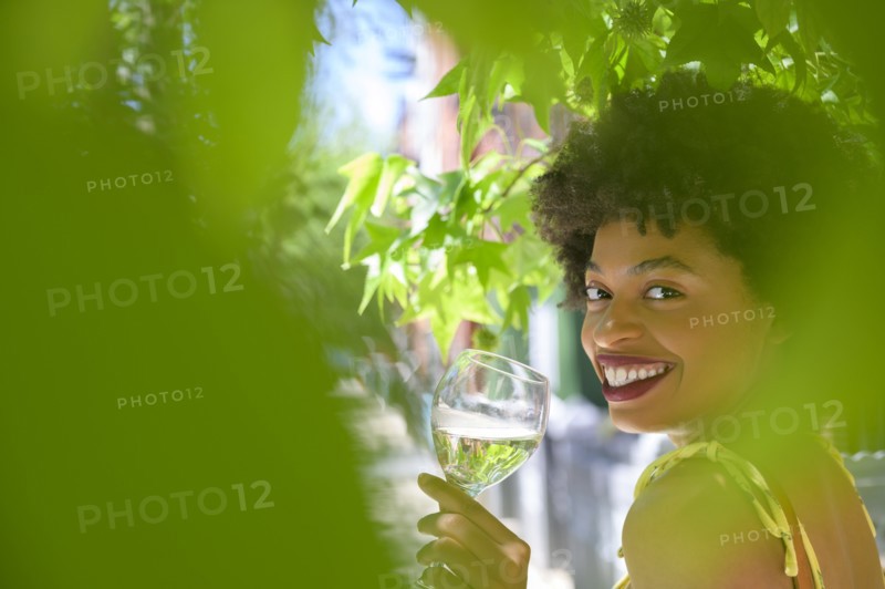 Smiling young woman with glass of white wine under tree