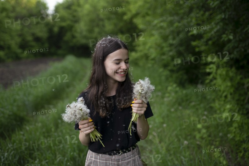 Smiling teenage girl holding dandelions in a field