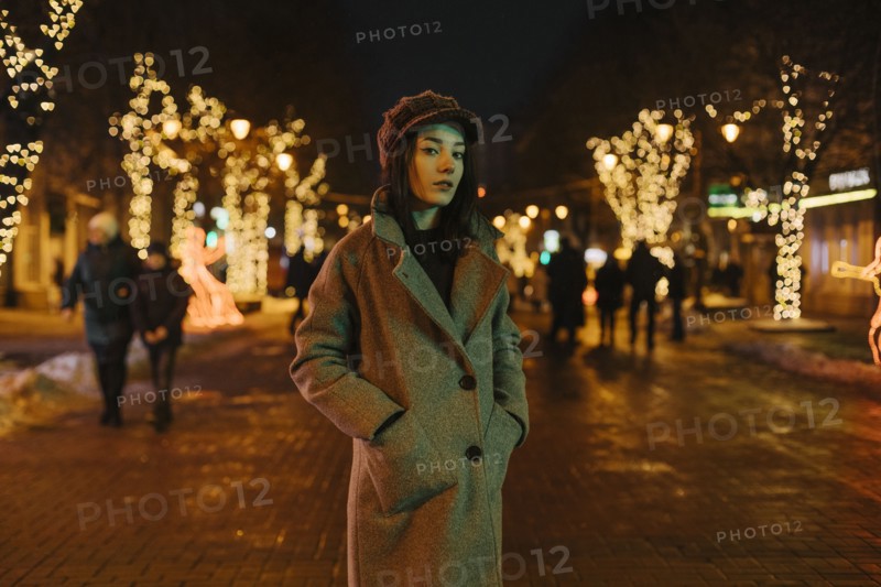 Young woman wearing coat on street at night with fairy lights