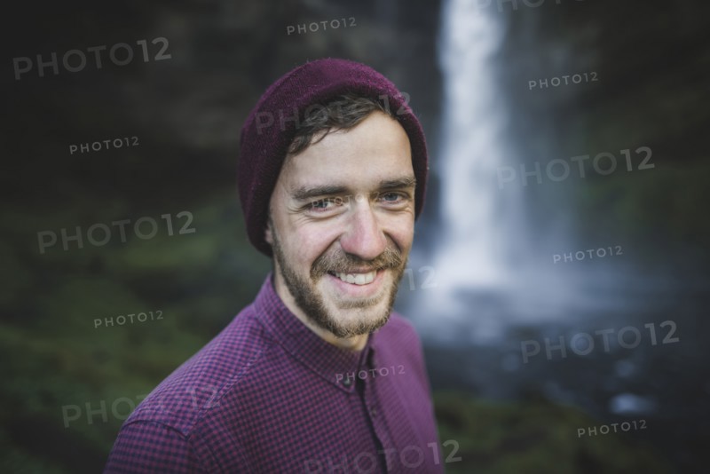 Portrait of smiling young man by Kvernufoss waterfall in Iceland