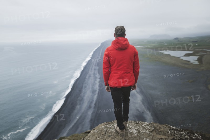 Man wearing red coat above beach in Vik, Iceland