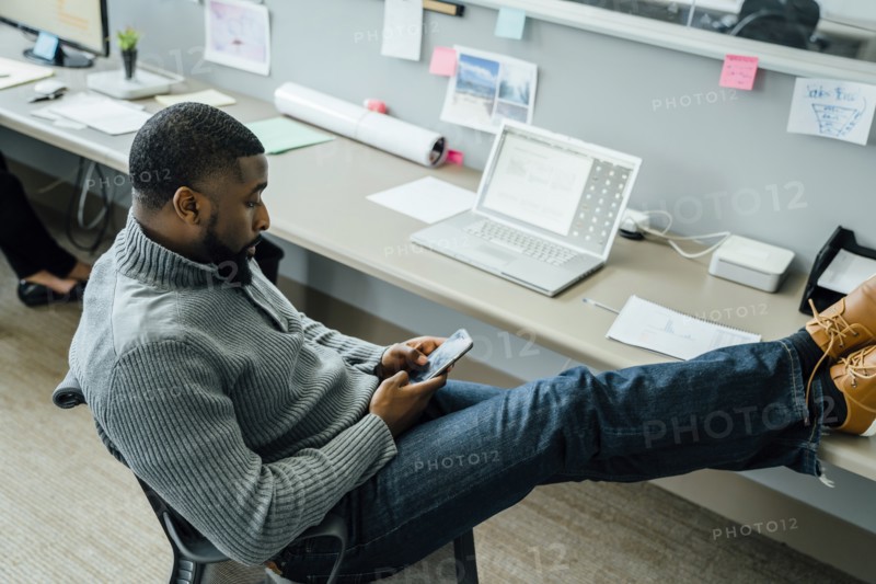 Man with his feet up using smart phone in office