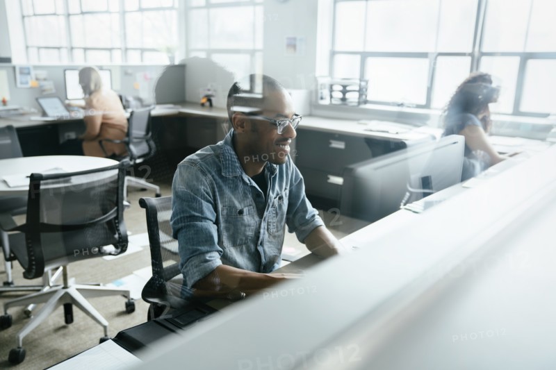 View through window of smiling man using computer in office