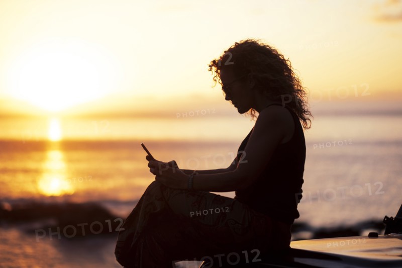 Woman using smart phone by beach at sunset