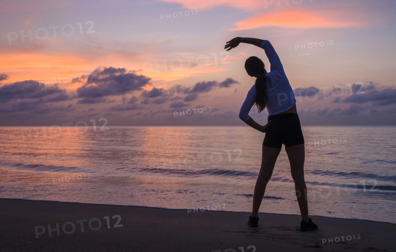 Woman practicing yoga on beach at sunset