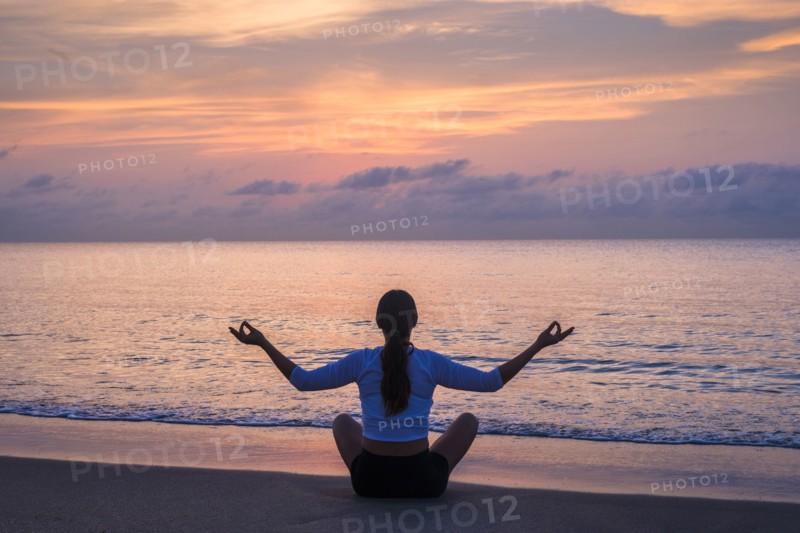 Woman practicing yoga on beach at sunset