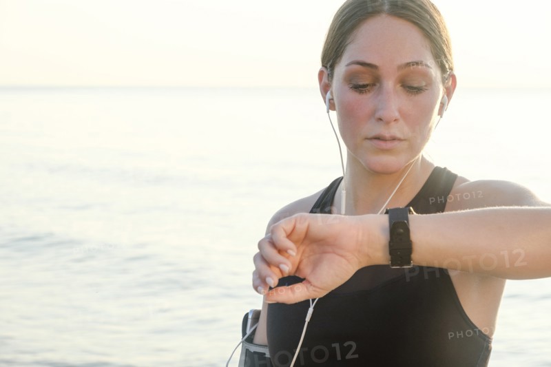Woman wearing headphones checking wrist watch on beach