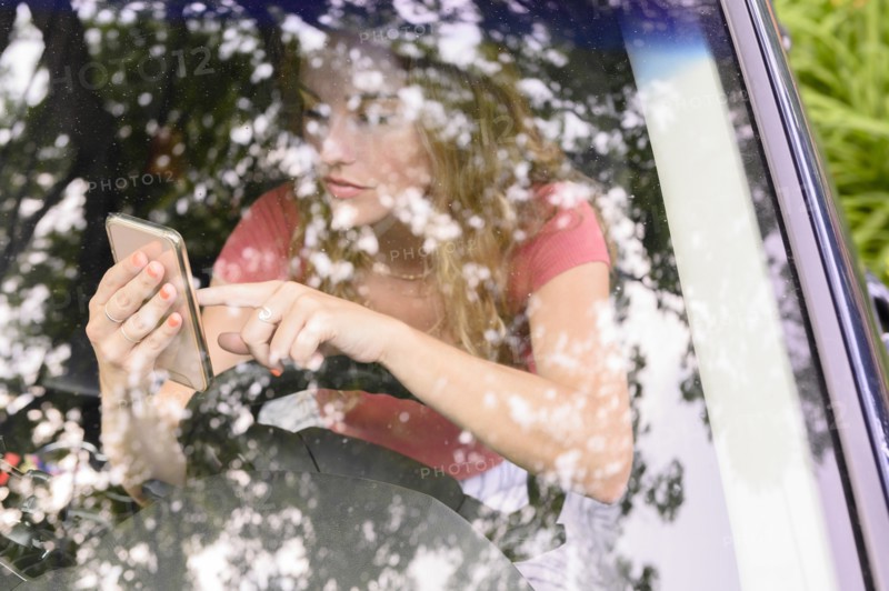View through car windscreen of young woman using smart phone