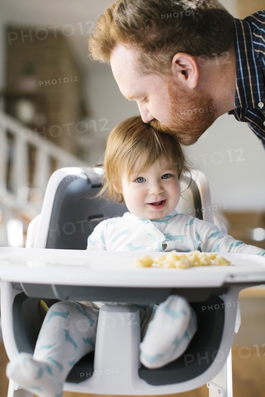 Father kissing head of his baby girl in high chair