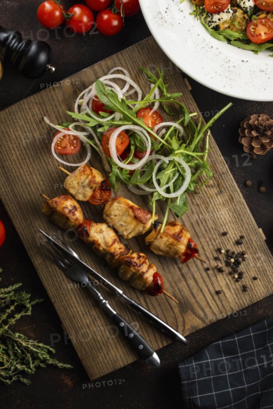 Grilled meat skewers and salad on cutting board