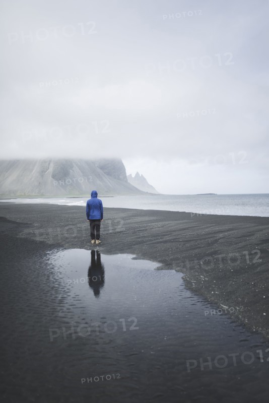 Man wearing blue coat on black sand beach in Kirkjubµjarklaustur