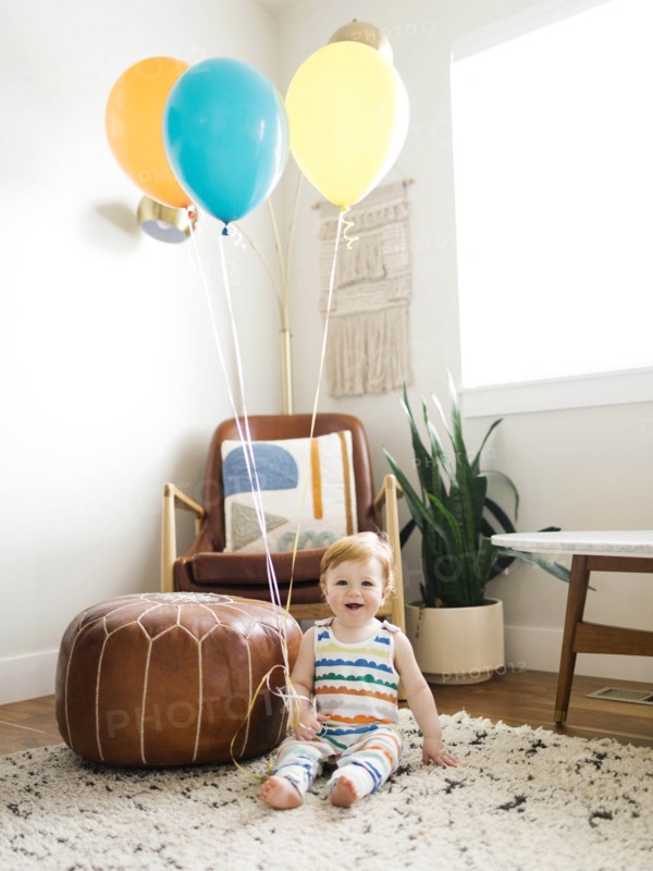 Baby boy holding balloons in living room