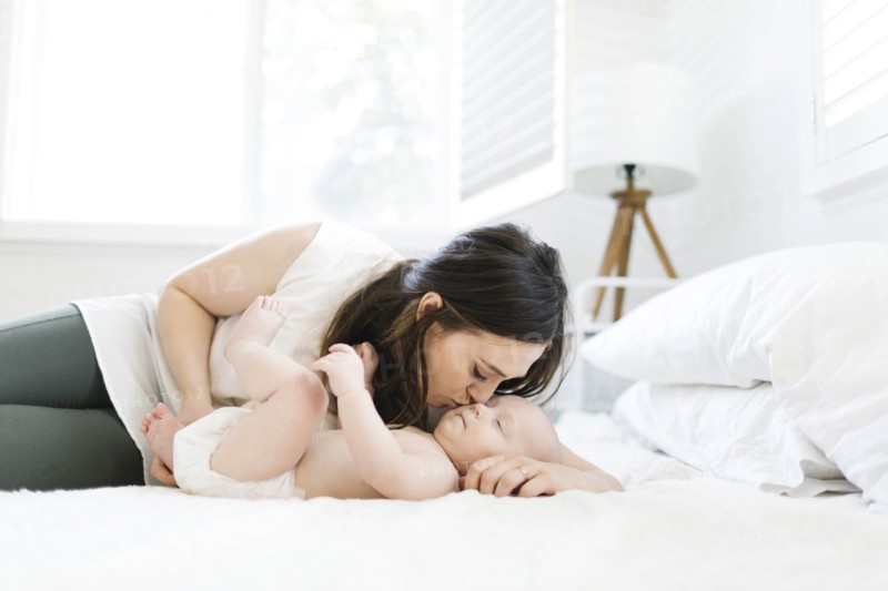 Mother kissing her son's cheek on bed