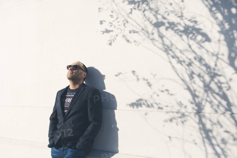 Man wearing sunglasses and blazer by white wall