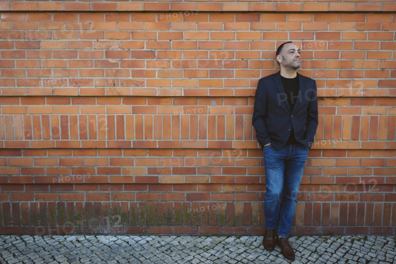 Man wearing blazer and jeans by brick wall