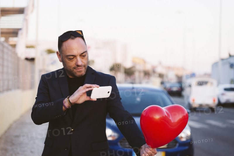 Man photographing red heart shaped balloon