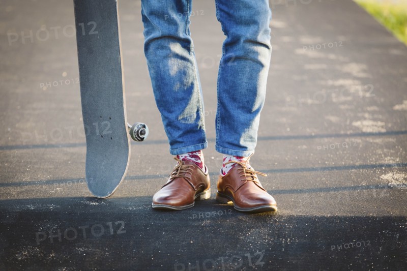 Feet of man with skateboard on footpath