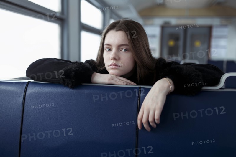 Young woman leaning on blue seat on train