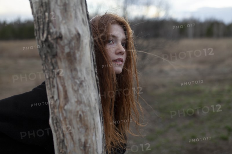 Windswept teenage girl by tree trunk