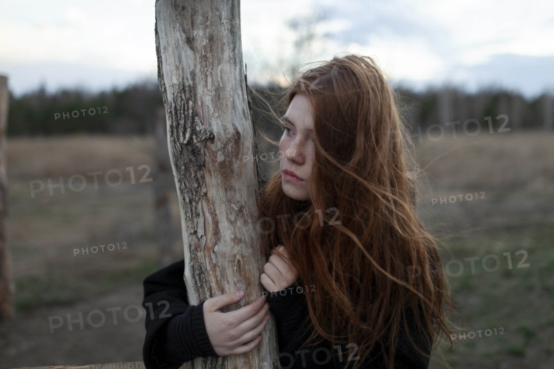Windswept teenage girl by tree trunk