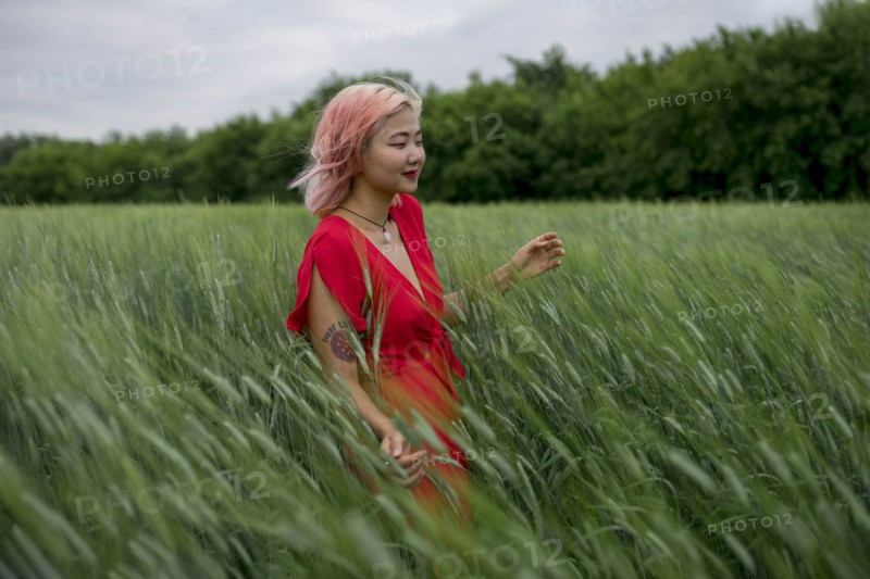 Woman with pink hair wearing red dress in wheat field