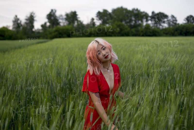 Woman with pink hair wearing red dress in wheat field