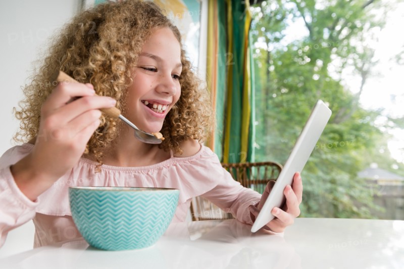 Smiling girl eating breakfast using tablet