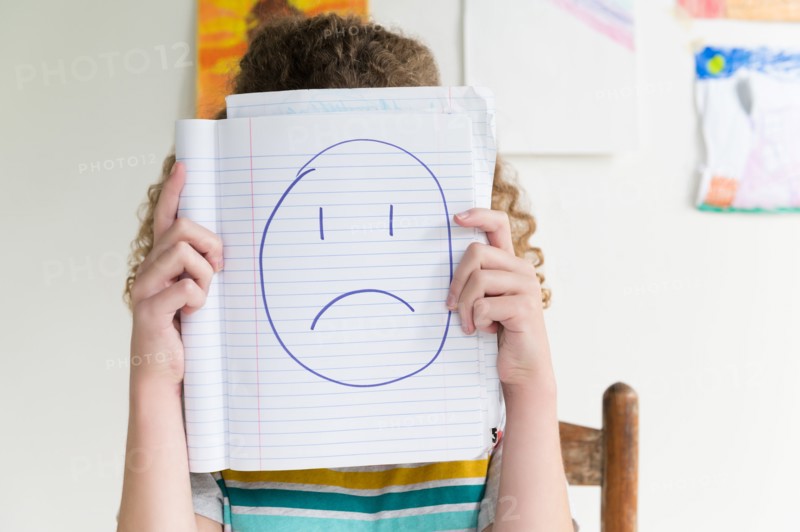 Girl holding note pad with drawing of sad face