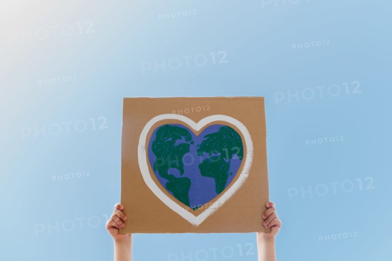 Young environmental activist holding sign against blue sky