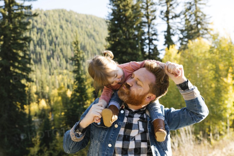 Father carrying his daughter on his shoulders by forest