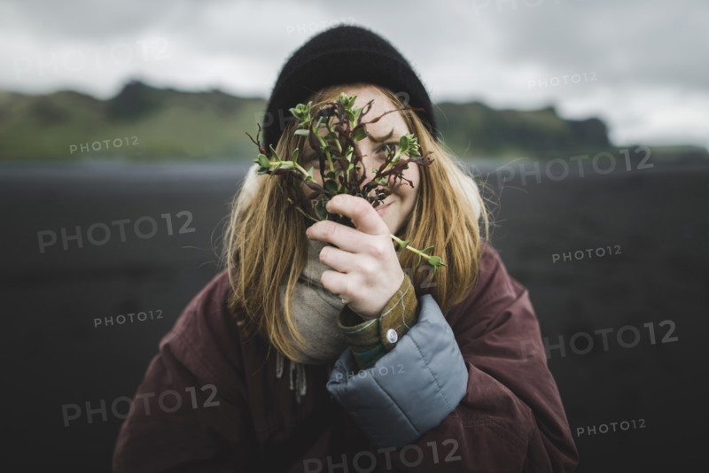 Woman holding plants over her face on beach