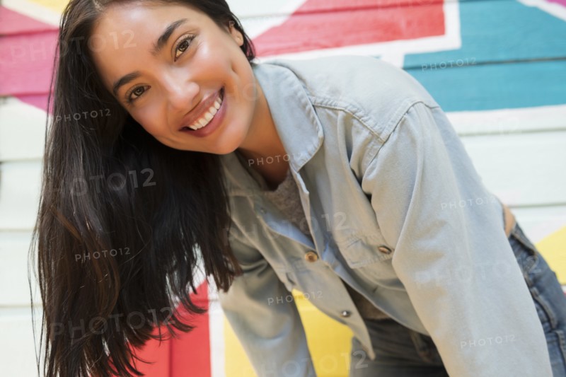 Smiling woman leaning forward against colorful wall